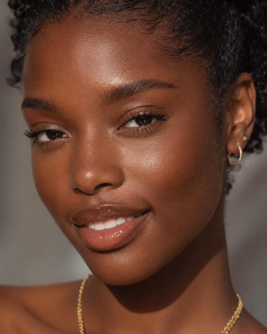 Close editorial portrait with softly glossy lips and a polished smile.