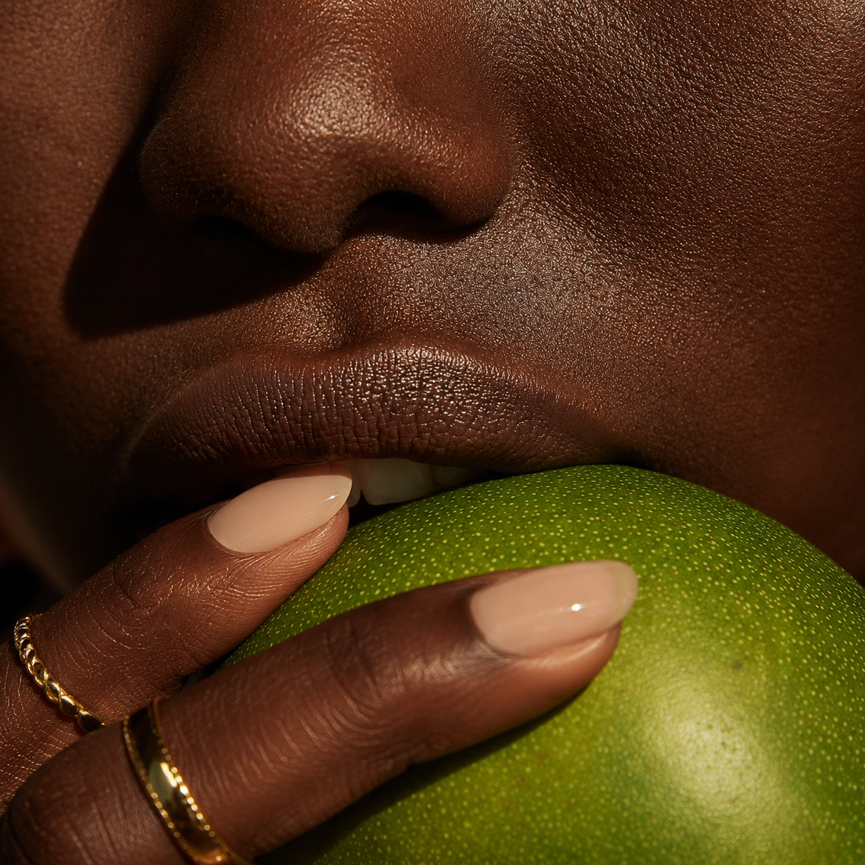 Close-up of softly lit lips, hand jewelry, and a green lime pressed at the mouth.