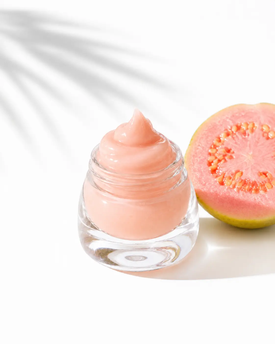 ButtahJam Guava whipped lip butter swirled in its glass jar beside a halved pink guava