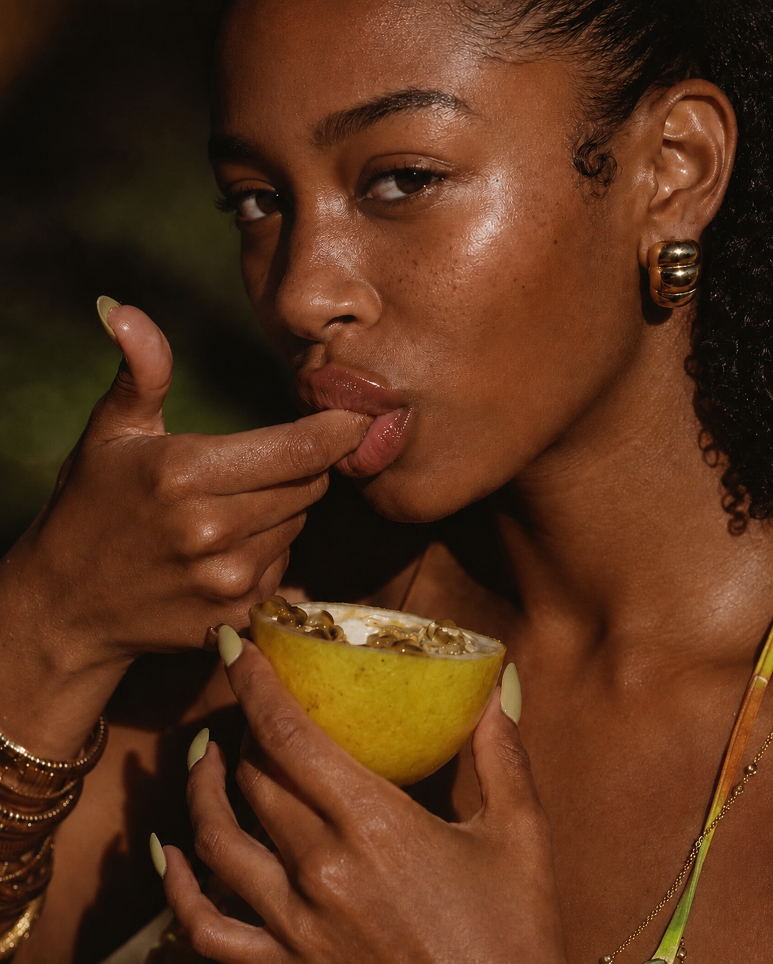 Close editorial portrait of glossy lips and passion fruit in warm evening light.